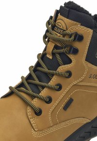 Bottine en daim marron avec des panneaux en maille noire, des lacets jaunes et noirs, et une semelle en caoutchouc noire. Comprend un patch logo et des œillets renforcés.