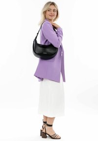 Bolso de hombro de cuero negro con forma curvada, que presenta una textura suave y un sutil detalle del logo. Llevado sobre un blazer lila claro y una falda blanca.