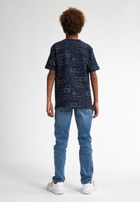 Camiseta de marinero con patrones geométricos de líneas blancas, combinada con jeans de mezclilla azul claro y zapatillas blancas. La vista trasera muestra un corte relajado.