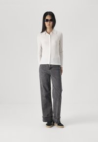 Light grey, long-sleeve button-up shirt in a ribbed texture, paired with loose-fitting dark grey jeans and black sneakers.