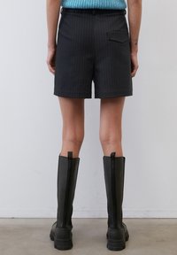 Černé pruhované šortky s rovnými nohavicemi, se zadní kapsou. Nosené s vysokými černými botami. Materiál vypadá hladký a přizpůsobený.