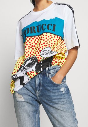 Osoba nosząca kolorową koszulkę Fiorucci z grafiką w stylu komiksowym i niemieckim napisem "Ich liebe dich", połączona z podartymi niebieskimi dżinsami.
