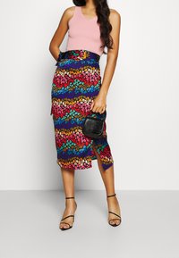 Jupe imprimée d'animaux multicolore au design mi-long, avec une fente latérale et une taille ajustée, associée à un haut rose à bords festonnés et un sac à main noir.