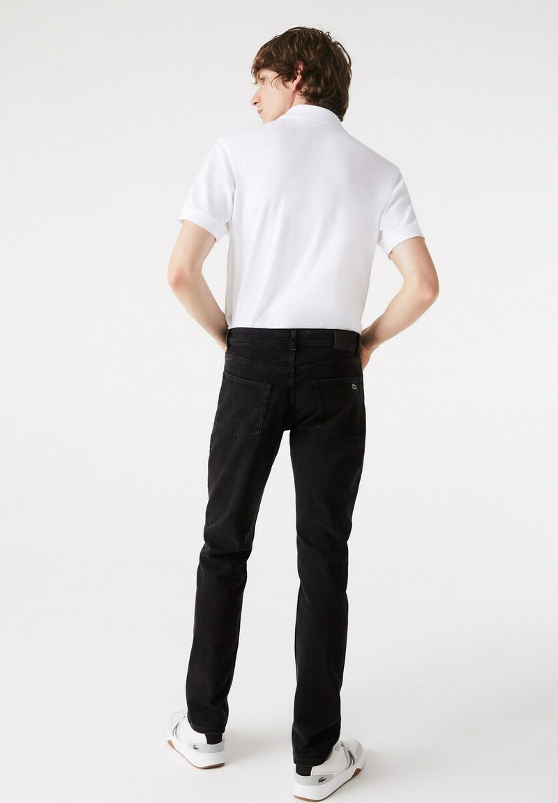 Weißes Polohemd, schwarze Jeans und weiße Sneakers. Die Jeans sind im Slim-Fit-Schnitt mit Gesäßtaschen und einem dezenten Logo. Angenehme Textur, lässiges Design.