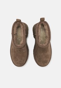 Botines de ante marrón con forro suave y esponjoso, punta redonda y tirador trasero para una fácil colocación. Parte superior texturizada y suela de goma duradera.