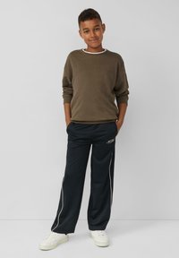 Oliwkowy sweatshirt z białym dekoltem, w parze z granatowymi spodniami dresowymi z białymi paskami bocznymi i logo. Białe sneakersy.