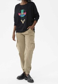 Sweatshirt noir oversize avec un design graphique coloré, associé à un pantalon cargo beige avec poches latérales et poignets élastiques. Mocassins noirs.