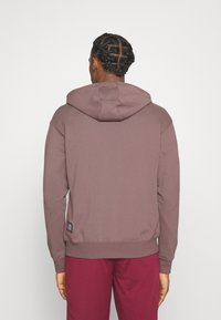 Hættetrøje i mauve med en afslappet pasform, ribbede manchetter og kant. Har et lille logo label på siden nær kanten.