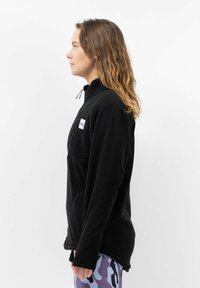 Zwarte fleece jack met een hoge kraag, een ritszak en zijzakken. Heeft een relaxte pasvorm en een zachte textuur, geschikt voor casual dragen.