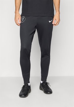 Black athletic pants made of smooth, stretchy fabric. Features a white Nike logo near the waist and a circular emblem on the thigh.