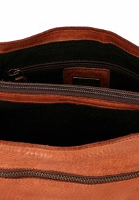 Interno di una borsa in pelle marrone con fodera in tessuto nero. Presenta una chiusura con cerniera e una tasca interna. Esterno testurizzato con cuciture visibili.