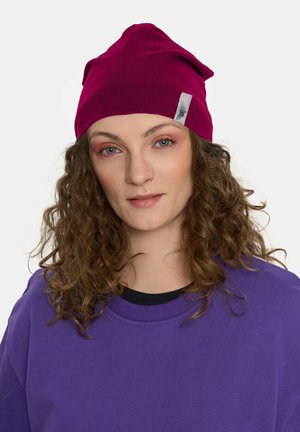 Bordowa dziana czapka z wyraźnym czubkiem i małą naszywką, noszona z fioletowym swetrem. Miękka tekstura i casualowy design.