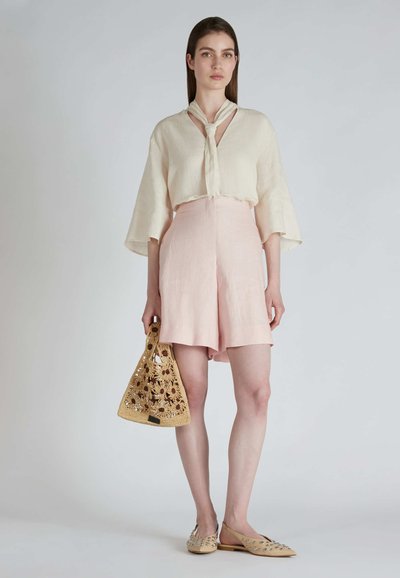 Leinenbluse mit Schleifendetail, rosa hochgeschnittene Shorts und einer geflochtenen gelben Handtasche. Slip-On-Schuhe mit Nieten verziert.