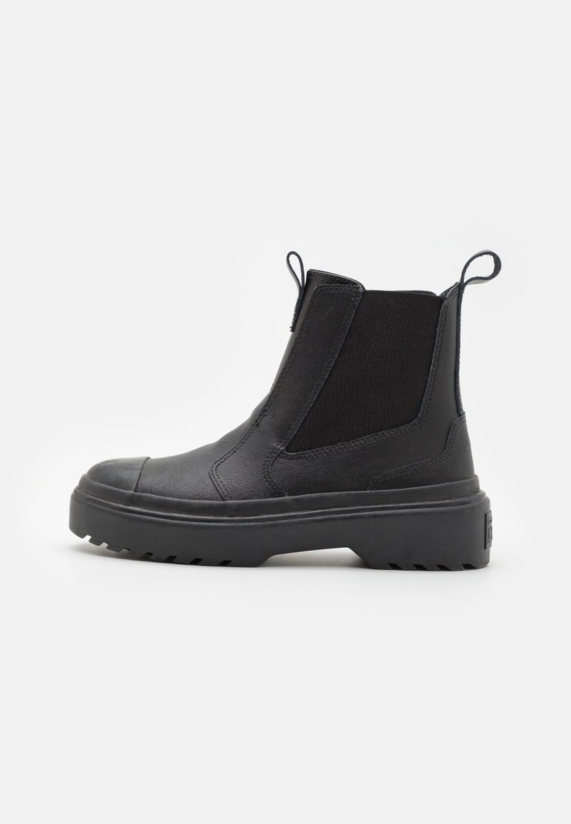 Botas Chelsea negras con un acabado texturizado, paneles laterales elásticos, tiradores y una suela de goma negra gruesa con un patrón de relieve.