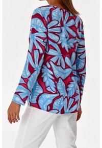 Bluzka z długim rękawem z jasnoniebieskim i magentowym wzorem liści na lekkim materiale, w luźnym kroju i okrągłym dekolcie.