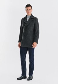 Ciemnoszara wełniana peacoat z podwójnym zapięciem, szerokim kołnierzem i dwiema kieszeniami, w zestawieniu z ciemnoniebieskimi dżinsami i czarnymi skórzanymi butami.