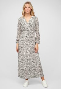 Robe maxi en tissu léger avec un motif de vagues noires sur fond crème, avec des manches longues et un design de corsage enveloppant.