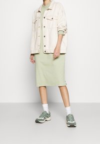 Kremowa dżinsowa kurtka, jasna zielona sukienka dzianinowa, białe skarpetki do kostek oraz zielone sportowe buty. Prosty design, sukienka o średniej długości, luźny krój.