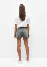 Pantalones cortos de denim gris con un dobladillo deshilachado y dos bolsillos traseros, combinados con una camiseta blanca de corte holgado. Modelo lleva sandalias de plataforma.