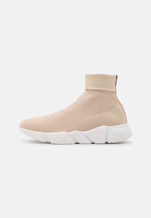 Beige stræksok-sneakers med hvid tyk gummisål og en foldet manchet øverst.