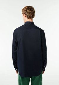 Camicia blu navy con colletto strutturato, maniche lunghe e una texture liscia; presenta un orlo curvo e polsini con bottone.