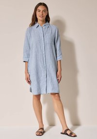 Abito camicia a righe blu con bottoni frontali, colletto e taschino sul petto. Maniche di lunghezza media e spacchi laterali, realizzato in tessuto leggero.