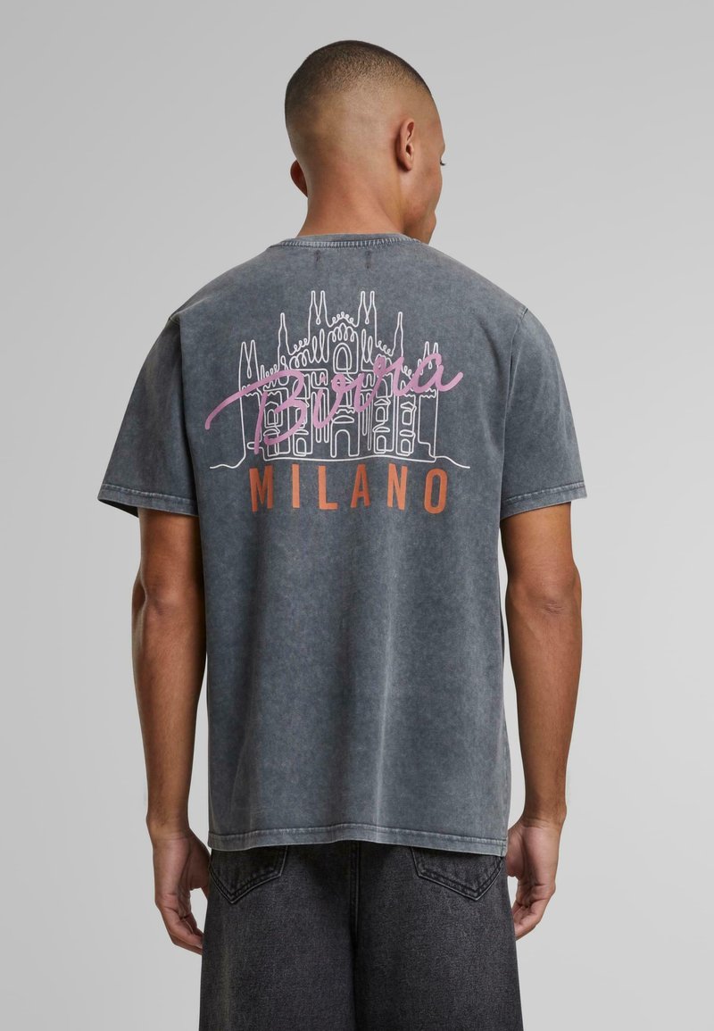 Pilkas medvilninis marškinėliai su grafika, vaizduojančia Duomo di Milano baltos ir rožinės spalvos, po ja spausdintas užrašas "Milano" oranžine spalva. Trumpomis rankovėmis, laisvo kirpimo.