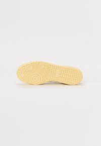 Rubber sneaker outsole, light yellow with textured grip pattern, circular details, and a smooth finish.