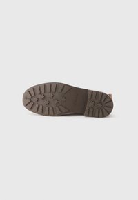 Semelle de chaussure marron foncé avec des rainures profondes et des semelles en forme d'étoile, estampillée "Clarks" sur un fond blanc.