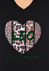 Černé tričko s designem srdce a různými leopardími vzory a slovy "LEO" zelenou barvou, přičemž pod tím je text "in love".
