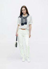 Fehér csíkos rövid ujjú ing, nyakban kötött tengerészkék sál, fehér farmer és fehér tornacipő. Fekete kézitáska texturált mintával.