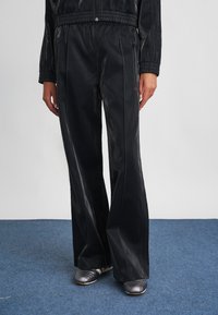 Μαύρο, γυαλιστερό, παντελόνι φαρδύς γραμμής από απαλό υλικό, με ελαστική μέση και διακριτική λεπτομέρεια επωνυμίας στο πλάι.