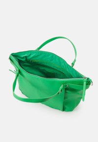 Sac en cuir vert avec fermeture éclair, large ouverture, sangle d'épaule réglable et poches intérieures pour l'organisation. Texture lisse et design simple.