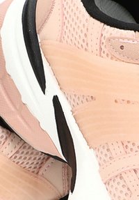 Zapatillas deportivas de color rosa claro, fabricadas en malla y material sintético, con una suela negra, acentos texturizados y un diseño aerodinámico.