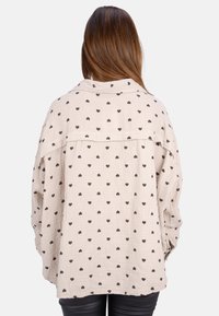 Beige pullover with an oversized design, featuring a textured fabric and black heart patterns. Includes a collared neckline and drop shoulders.
