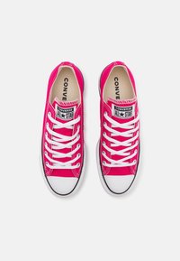 Baskets en toile roses avec semelles en caoutchouc blanches, embouts noirs et lacets blancs. Présente un logo "Converse All Star" visible sur la languette.
