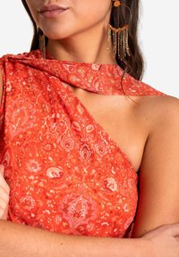 Vestido rojo con un diseño de un solo hombro, que presenta motivos florales y acentos metálicos. La tela texturizada cae elegantemente sobre el hombro.