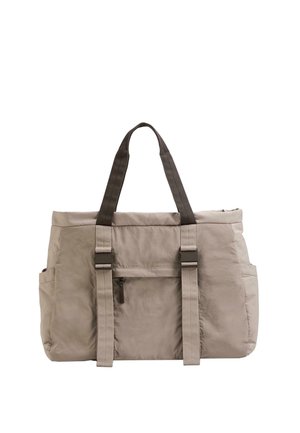 Borsa tote beige con manici scuri, tasca frontale con cerniera, tasche laterali e due cinturini regolabili con fibbia sul davanti.