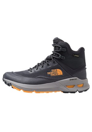 Scarpa da trekking alta nera e grigia con logo arancione, dettagli arancioni sulla suola e lacci neri, progettata per l'uso all'aperto.