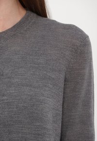 Grauer Strickpullover mit Rundhalsausschnitt, der eine glatte Textur und eine taillierte Silhouette aufweist. Der Stoff wirkt weich und leicht.