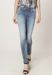 Vaqueros ajustados de color azul claro con un acabado desgastado, que cuentan con cinco bolsillos, una cintura de altura media y detalles decorativos de trenzado negro en los puños.