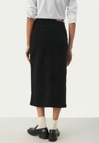 Henkilö, jolla on valkoinen paita, musta midihame takataskuilla, kermaiset sukat ja mustat korolliset loafer-kengät, seisoo yksinkertaisella taustalla.