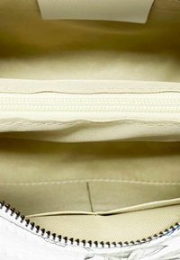 L'interno della borsa bianca presenta una fodera in tessuto beige liscia con una tasca con zip. I punti di cucitura appaiono uniformi e i bordi metallici della cerniera sono visibili.