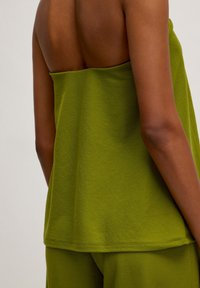 Grünes ärmelloses Oberteil mit lockerer Passform, aus strukturiertem Stoff und mit geradem Saum, der teilweise den Rücken bedeckt.