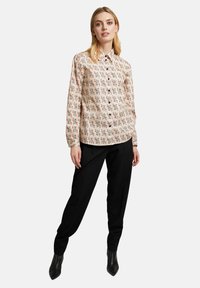 Langärmliges Button-up-Hemd in Creme mit mehrfarbigem Muster. Verfügt über einen klassischen Kragen und wird mit schwarzen Hosen und Ankle Boots kombiniert.