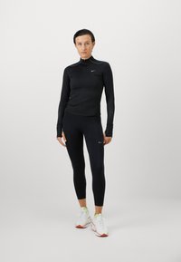 Czarna, długorękawowa koszulka sportowa z zamkiem błyskawicznym, dopasowane legginsy i białe sneakersy z kolorowymi akcentami. Posiada perforowane detale na rękawach.