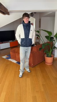 La giacca presenta una parte superiore in pile bianco con una parte inferiore trapuntata color navy, abbinata a jeans azzurri e sneakers argento. Ambientazione interna con piante.