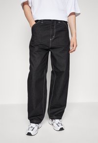 Pantalones de mezclilla negra con un ajuste holgado, que presentan costuras blancas, bolsillos frontales y un diseño de corte recto. Combinados con zapatillas blancas.