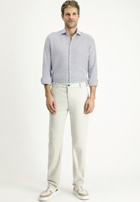 Camicia a maniche lunghe a fantasia blu chiaro abbinata a pantaloni crema e sneakers bianche. L'outfit presenta una vestibilità slim e colletto con bottoni.