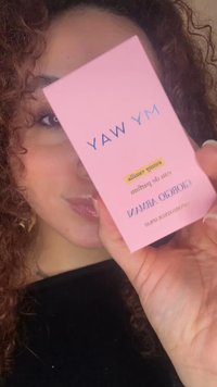Femme aux cheveux bouclés tenant près de son visage une boîte rose de parfum Giorgio Armani My Way, couvrant partiellement un œil.